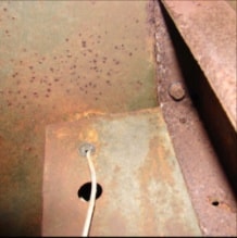Rusted halftrack dash panel corner with wiring hole and metal surface detail