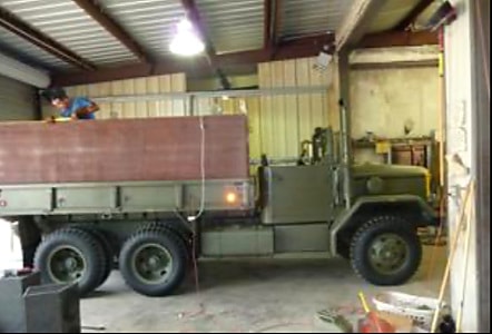 Deuce-and-a-Half in workshop with person on top driving through door